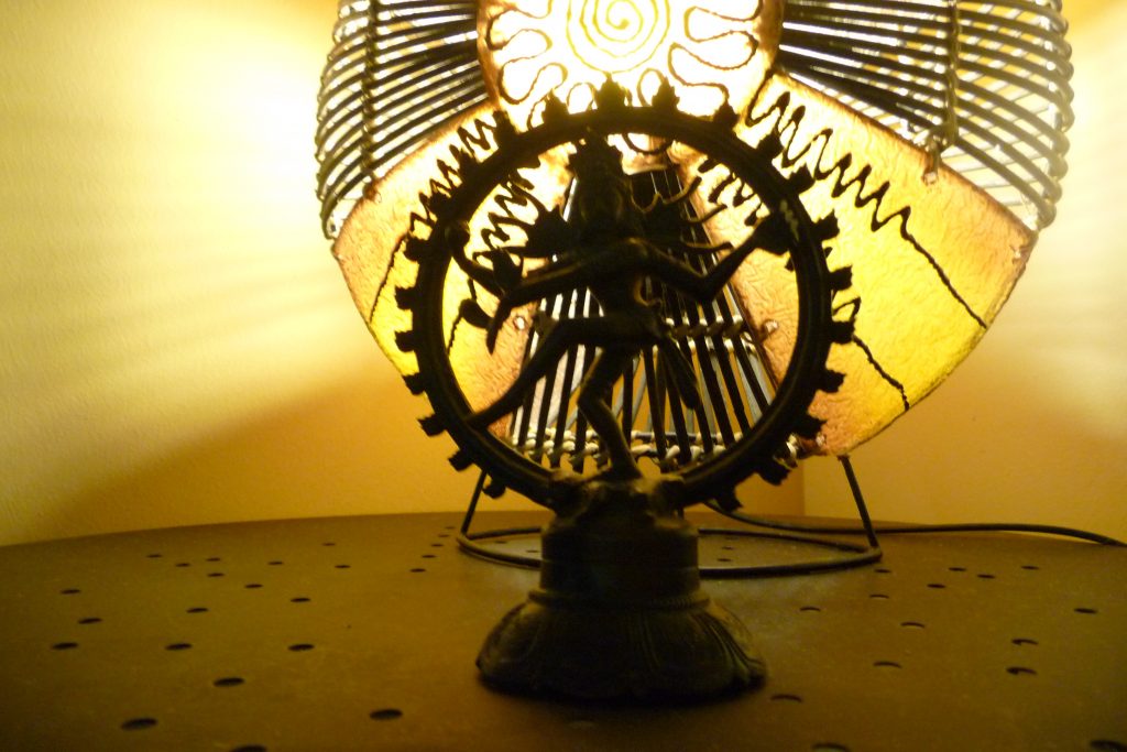 Shiva, der indische Gott der für Entstehen und Vergehen tanzt in einer strahlenden Sonne beleuchtet von einer im Hintergrund leuchtenden Lampw