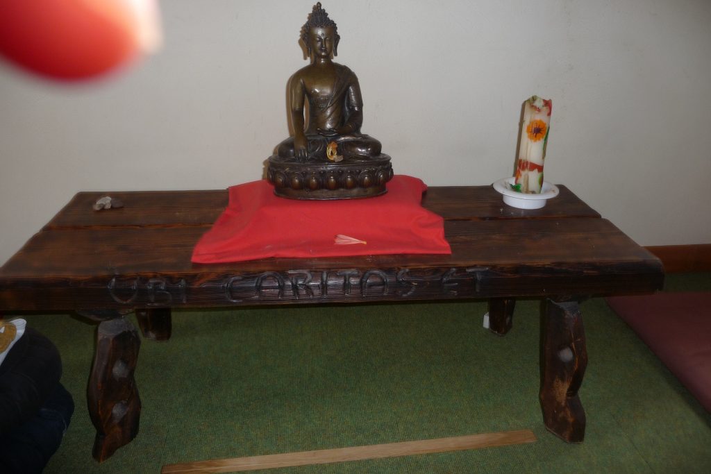 Ein kleiner Holzaltar mit Kerze rechts und in der Mitte eine Buddhastatue auf rotem Tuch